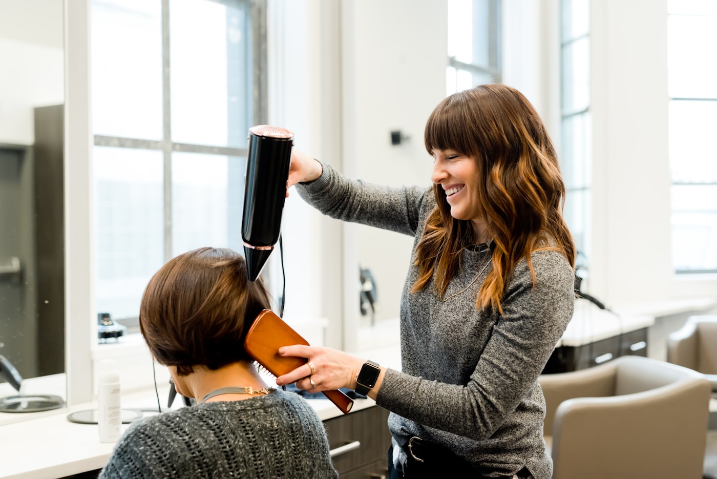 A stylist at Alder and Ash blow-drying a client's hair in a bright Laramie salon