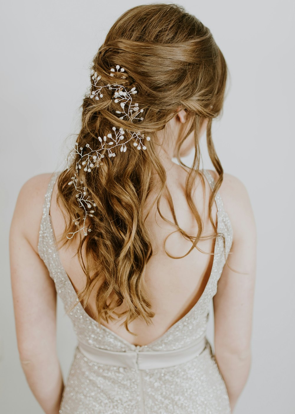 Bridal half-up style with soft waves and a pearl hair vine, seen from behind
