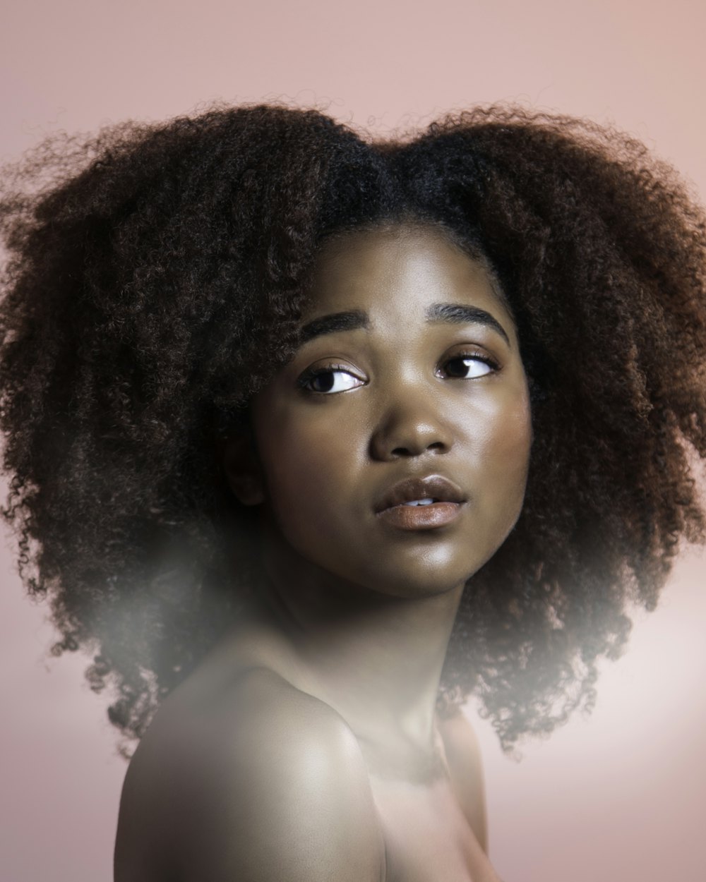 Defined natural curls with a soft rounded shape, photographed against a pink backdrop